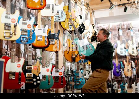 Crispin Weir, copropriétaire de Regent Sounds, tient une guitare exposée dans le célèbre magasin de guitare et studio de musique Denmark Street qui relance après une rénovation majeure dans le centre de Londres. Date de la photo : mercredi 24 septembre 2025. Banque D'Images