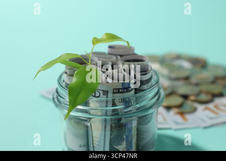 Pot en verre avec dollars, germe et pièces de monnaie sur fond bleu clair, gros plan Banque D'Images