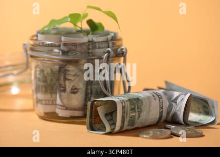 Pot en verre avec dollars, pièces de monnaie et germe sur fond orange pâle, gros plan Banque D'Images