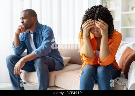 Triste couple noir assis à part sur le canapé à la maison, femme tenant la tête Banque D'Images