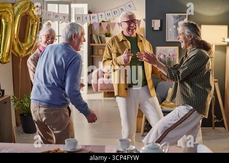 Groupe d'amis seniors riant et dansant à la fête d'anniversaire Banque D'Images