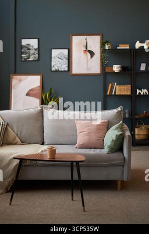 Intérieur moderne du salon avec canapé gris clair avec coussins pastel, table basse en bois tenant une tasse en céramique, art mural abstrait et étagère en arrière-plan Banque D'Images