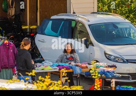 Vue rapprochée de deux femmes à la vente de cour avec des tables de vêtements près de voiture blanche garée en journée ensoleillée. Suède. Banque D'Images