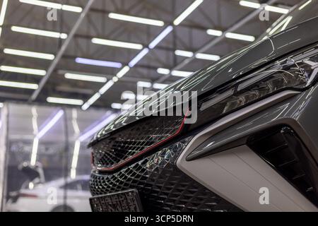 Vue rapprochée de l'avant de la voiture grise élégante mettant en évidence le phare et la calandre dans un studio d'esthétique intérieure. L'éclairage artificiel accentue la surface brillante Banque D'Images