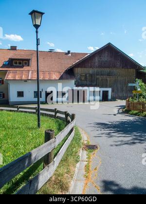 Vue idyllique sur le village avec une grange résidentielle à une jonction de route en pente avec lanterne, clôture en bois et panneau indiquant Faistenoy. Banque D'Images