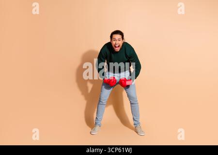 Jeune homme portant des gants de boxe rouges dans une tenue décontractée posant joyeusement sur un fond beige Banque D'Images