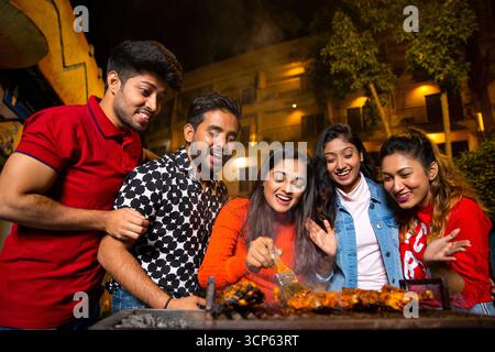 Heureux groupe de jeunes amis profitant d'une fête barbecue la nuit Banque D'Images
