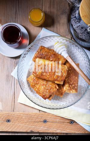 Crêpes avec fromage cottage et garniture aux raisins secs, servies avec miel et thé noir. Gâterie traditionnelle pour Maslenitsa ou Carnaval. Style rustique, selectiv Banque D'Images