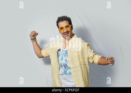 Homme excité et énergique en lunettes de soleil posant avec un sourire joyeux Banque D'Images