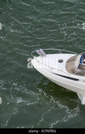 Une vue en grand angle capture la proue d'un bateau à moteur de croisière à cabine blanche alors qu'il se déplace dans l'eau sombre et agitée, avec des ailes bleues fixées au rail. Banque D'Images