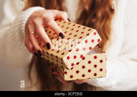 Boîte cadeau ouverture par femme. Mains tenant paquet festif avec des étoiles. Concept surprise des fêtes. Gros plan du déroulement actuel. Banque D'Images