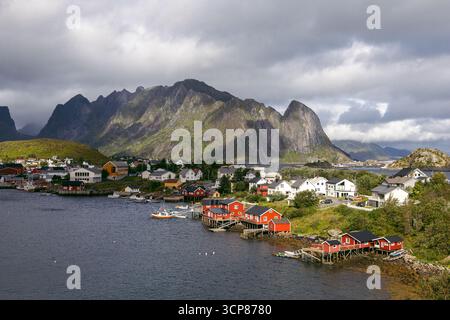 Village de pêcheurs Reine avec des cabanes traditionnelles de rorbu rouge le long du front de mer, entouré de pics montagneux spectaculaires dans les îles Lofoten, en Norvège. Banque D'Images