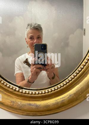 Femme d'âge moyen avec les cheveux gris regardant dans un miroir tout en prenant un selfie Banque D'Images