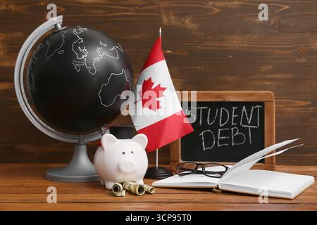 Tirelire avec argent, globe, drapeau canadien et livre sur table en bois. Concept d'endettement étudiant Banque D'Images