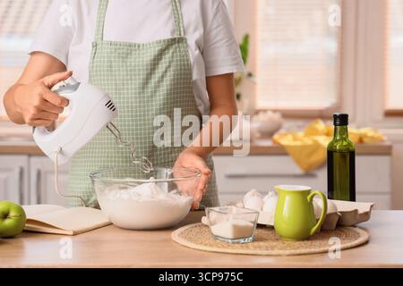 Femme fouettant des blancs d'oeufs avec mélangeur dans la cuisine Banque D'Images