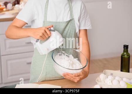 Femme fouettant des blancs d'oeufs avec mélangeur dans la cuisine Banque D'Images