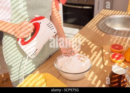 Femme fouettant des blancs d'oeufs avec mélangeur dans la cuisine Banque D'Images