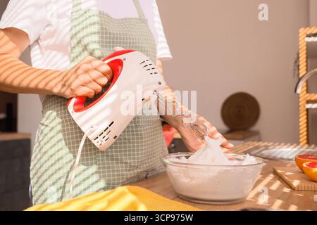 Femme fouettant des blancs d'oeufs avec mélangeur dans la cuisine Banque D'Images