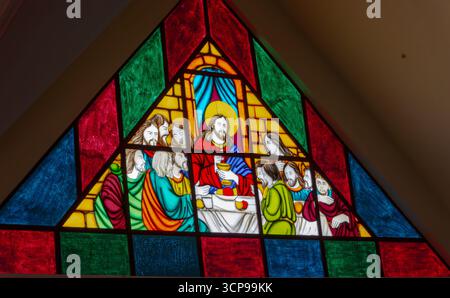 Vitrail triangulaire représentant Jésus et les douze disciples à la dernière Cène avec des panneaux de verre rouge vif, vert et bleu Banque D'Images
