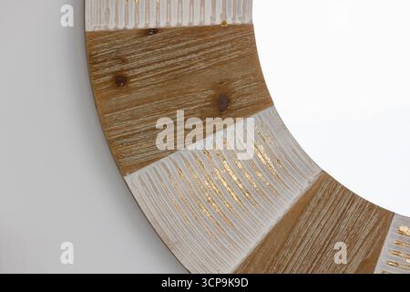 Gros plan d'un cadre de miroir décoratif circulaire présentant une alternance de panneaux en bois et de sections texturées blanches avec des accents dorés. Parfait pour mod Banque D'Images