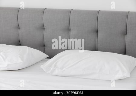 Un lit soigneusement fait dispose d'une tête de lit grise douce et d'oreillers blancs, créant une scène de chambre calme et minimaliste adaptée à la décoration d'intérieur, les hôtels et les lif Banque D'Images
