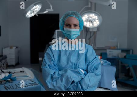 Chirurgienne debout en salle d'opération portant une blouse bleue organisant les outils sous les lumières chirurgicales Banque D'Images