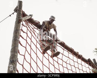 Soldat homme afro-américain grimpant filet rouge obstacle course poutre de préhension et jambes de levage Banque D'Images