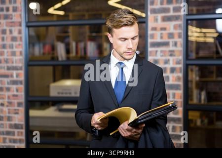 L'homme examine des papiers dans un espace de bureau moderne avec étagères en verre, dossier jaune et imprimante Banque D'Images