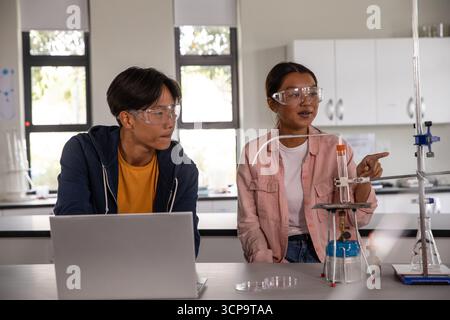 Étudiants asiatiques portant des lunettes de sécurité, menant des expériences au laboratoire avec un ordinateur portable et un tube à essai Banque D'Images