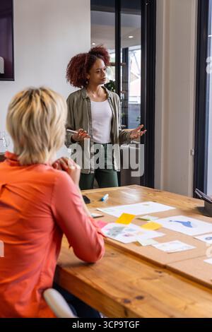 Diverses collègues féminines discutant des maquettes de conception autour de la table de conférence dans la salle de réunion Banque D'Images