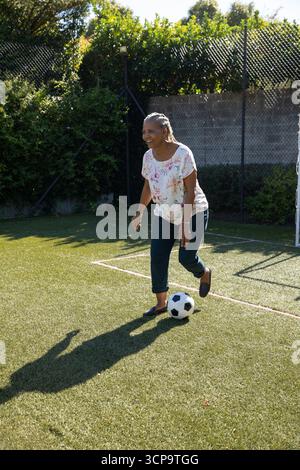 Femme afro-américaine senior équilibrant et contrôlant le ballon de football noir et blanc sur le terrain Banque D'Images