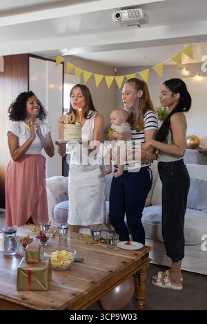 Diverses amies féminines célébrant le 30e anniversaire dans le salon avec des lumières de chaîne, gâteau Banque D'Images