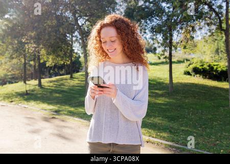 jeune femme aux cheveux roux bouclés à l'aide d'un téléphone portable Banque D'Images