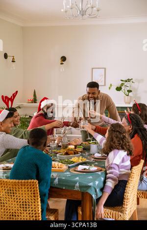 Famille afro-américaine partageant un repas de vacances à la table de la salle à manger, au centre de la dinde rôtie Banque D'Images