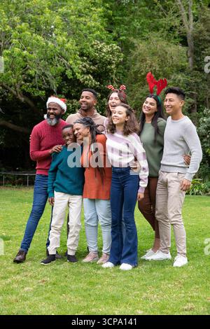 Famille diverse debout sur l'herbe dans le parc portant chapeau de père noël, arc de canne de bonbon, bois de renne Banque D'Images