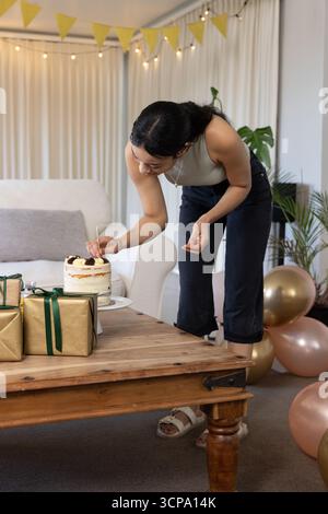 Femme asiatique plaçant des fleurs décoratives sur le gâteau sur la table basse dans le salon, bannière fanion Banque D'Images