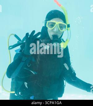Plongée sous-marine signale OK sous l'eau avec masque de plongée jaune et régulateur dans la piscine turquoise Banque D'Images