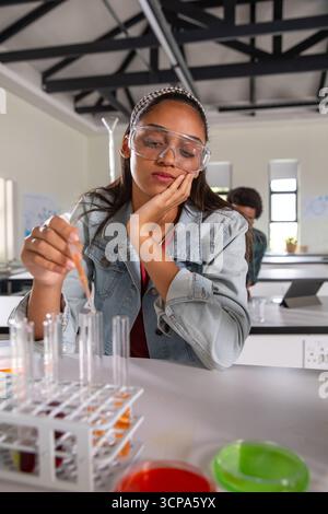 Étudiante adolescente hispanique tenant compte d'un compte-gouttes en plastique au-dessus du support de tubes à essai au laboratoire de chimie de l'école Banque D'Images