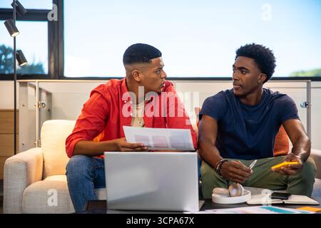 Divers collègues masculins collaborant dans le salon examinant des documents et smartphone sur la table basse Banque D'Images