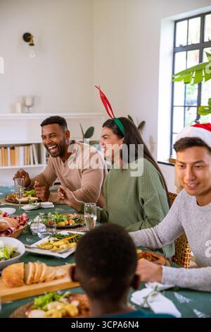 Divers amis discutant autour de la table dans la salle à manger avec nappe de flocon de neige, verres à vin Banque D'Images
