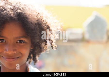 Garçon afro-américain souriant à l'extérieur près du mur peint sous la lumière du soleil, espace de copie Banque D'Images