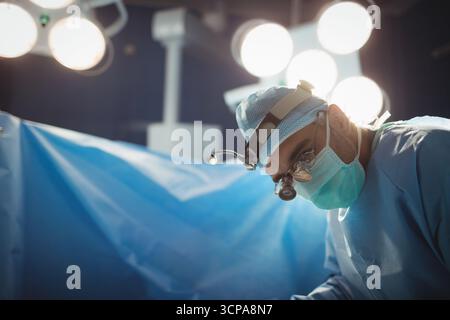 Chirurgien vêtu de sexe masculin dans OU utilisant une loupe penchant sur le patient sous un champ lumineux, espace de copie Banque D'Images