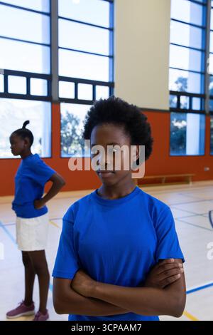 Filles afro-américaines en vêtements de sport se tenant à part dans le gymnase avec banc, lignes de cour visibles Banque D'Images