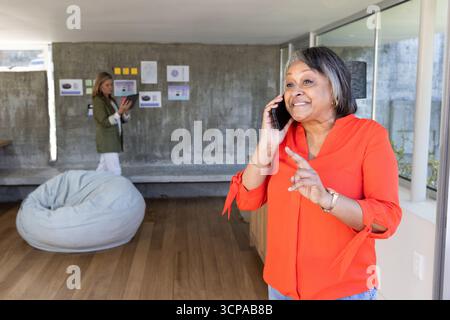 Diverses collègues féminines parlant sur smartphone tout en analysant des graphiques à la maison, copiez l'espace Banque D'Images