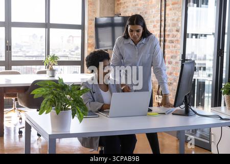 Diverses collègues féminines collaborant sur le projet à l'aide d'un ordinateur portable, moniteur au bureau Banque D'Images