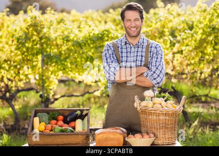 Agriculteur présentant caisse de légumes, panier de pommes de terre et champignons, pain, œufs sur table dans le vignoble Banque D'Images
