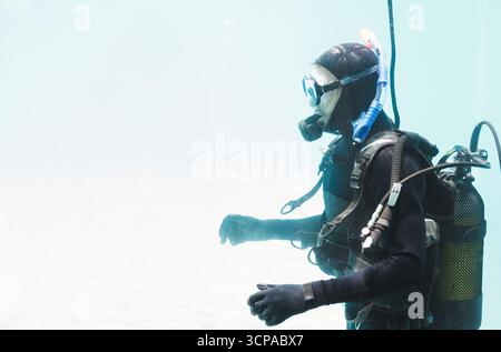 Plongeur portant un équipement de plongée complet avec masque, régulateur et BCD dérivant dans l'eau bleu-vert clair Banque D'Images
