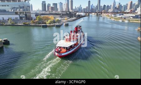 Brooklyn, États-Unis - 13 août 2023 : vue aérienne d'un bateau rouge vif traversant l'East River en direction de l'emblématique skyline. Banque D'Images