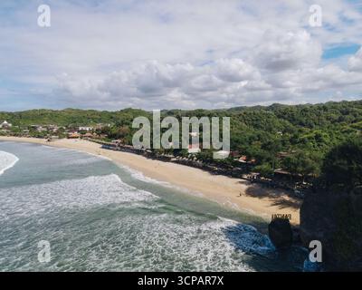 Vue aérienne de la bande côtière vibrante où la mer turquoise rencontre les sables dorés sous un ciel strié de nuages blancs doux, Yogyakarta, Indonésie. Banque D'Images