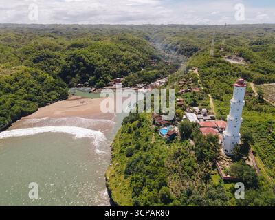 Vue aérienne d'un phare blanc debout près de l'embouchure d'une rivière, entouré d'une forêt verdoyante, Java, Indonésie. Banque D'Images